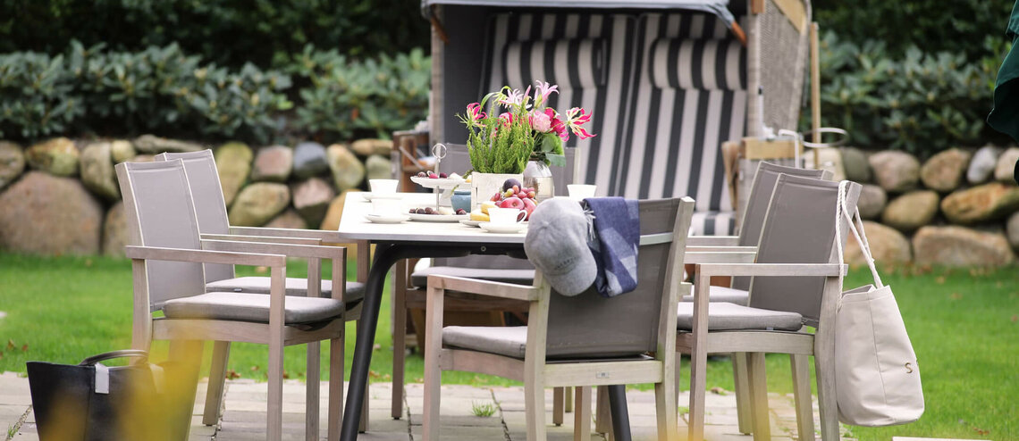 Gedeckter Gartentisch mit Blumen und Strandkorb im Hintergrund im Severin*s Resort & Spa auf Sylt.