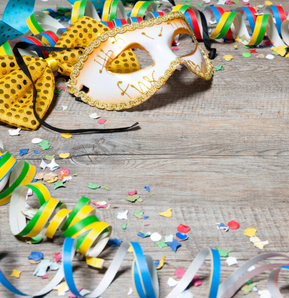 Angebot "Narrenfreie Auszeit" l Severin*s Resort & Spa Sylt Karnevalsmaske mit goldenen Details, bunte Luftschlangen und Konfetti auf Holztisch.