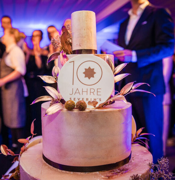 Eine Torte mit Dekoration mit der Aufschrift "10 Jahre Severin*s". Im Hintergrund stehen viele Menschen