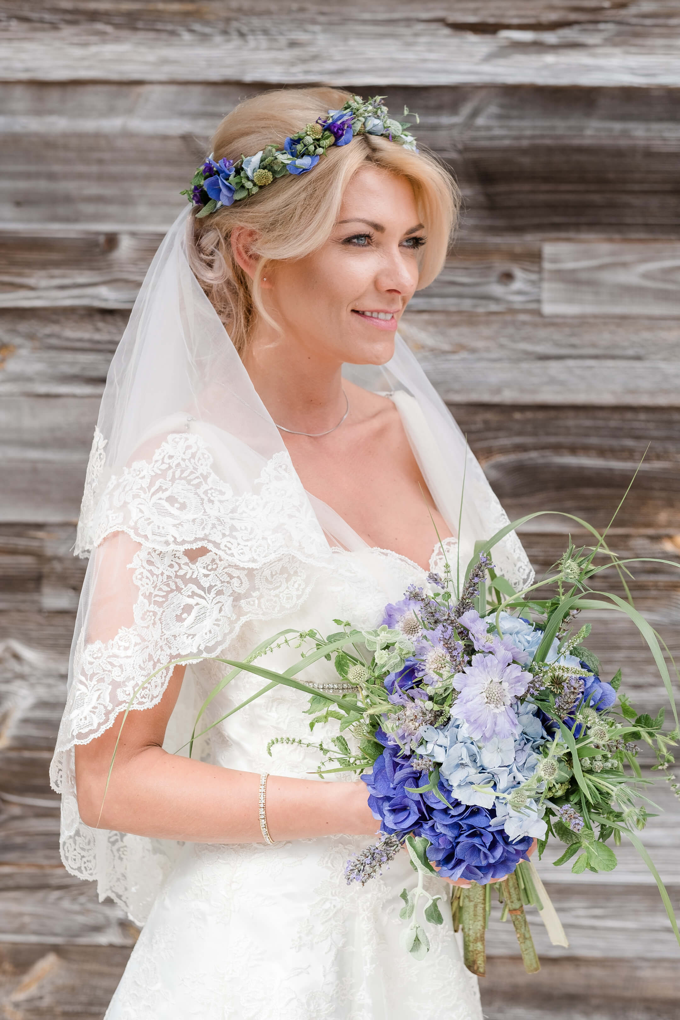 Braut mit Blumenstrauß und Spitzenkleid vor Holzwand, Severin*s Resort & Spa, Sylt.