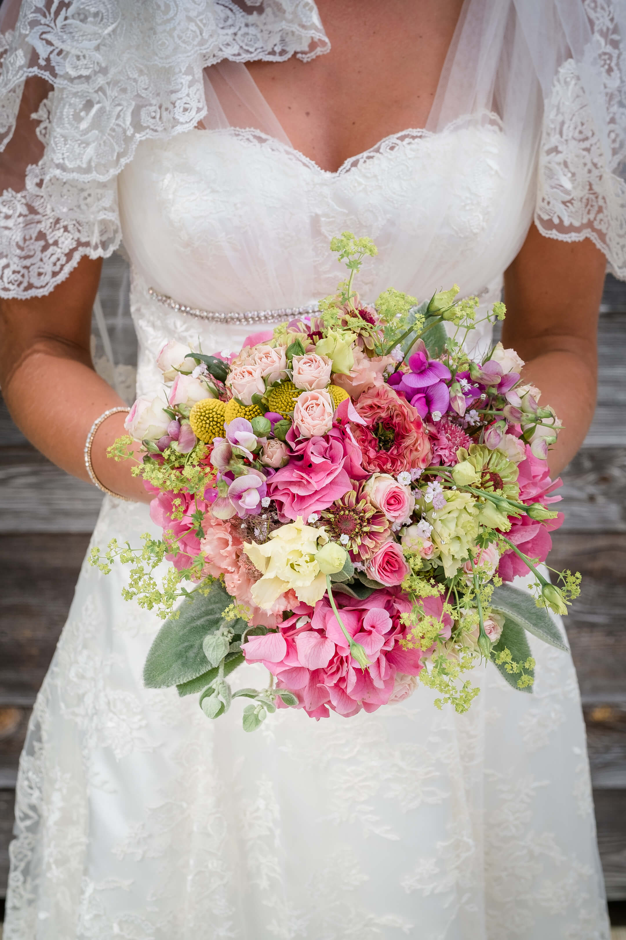 Braut in Spitzenkleid hält bunten Blumenstrauß, perfekt für Hochzeiten im Severin*s Resort & Spa auf Sylt.