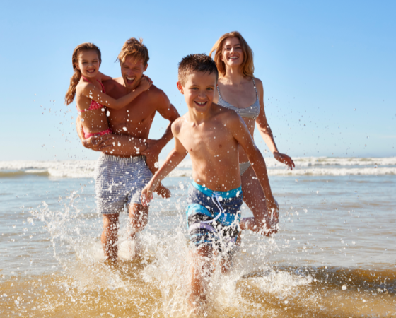 Familie genießt den Strand bei Sonnenschein, im flachen Wasser spielend, vor blauem Himmel und sanften Wellen.