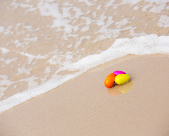 Bunte Steine liegen am Sandstrand, umspült von sanften Wellen.