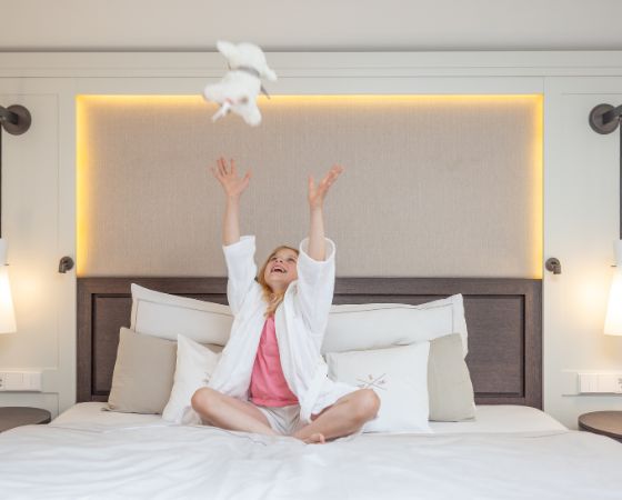 Kind sitzt auf dem Bett und wirft Kuscheltier in die Luft - Severin*s Resort & Spa