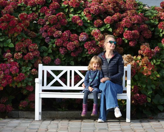 Frau und Kind sitzen auf einer weißen Bank vor einem blühenden Hortensienbusch - Severin*s Resort & Spa