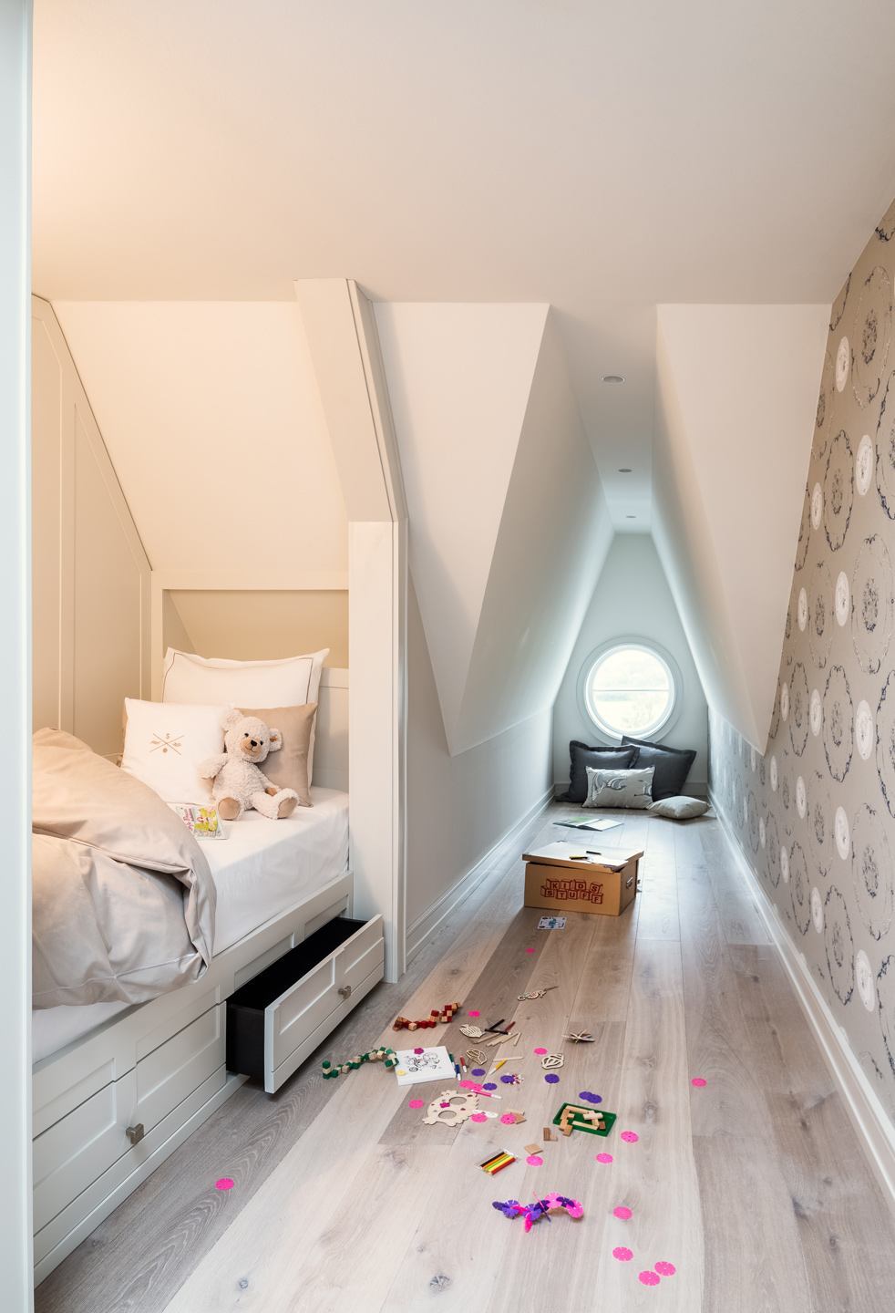 Helles Kinderzimmer mit Einzelbett, Kuscheltier, Spielzeug auf dem Boden und rundem Fenster im Severin*s Resort & Spa.