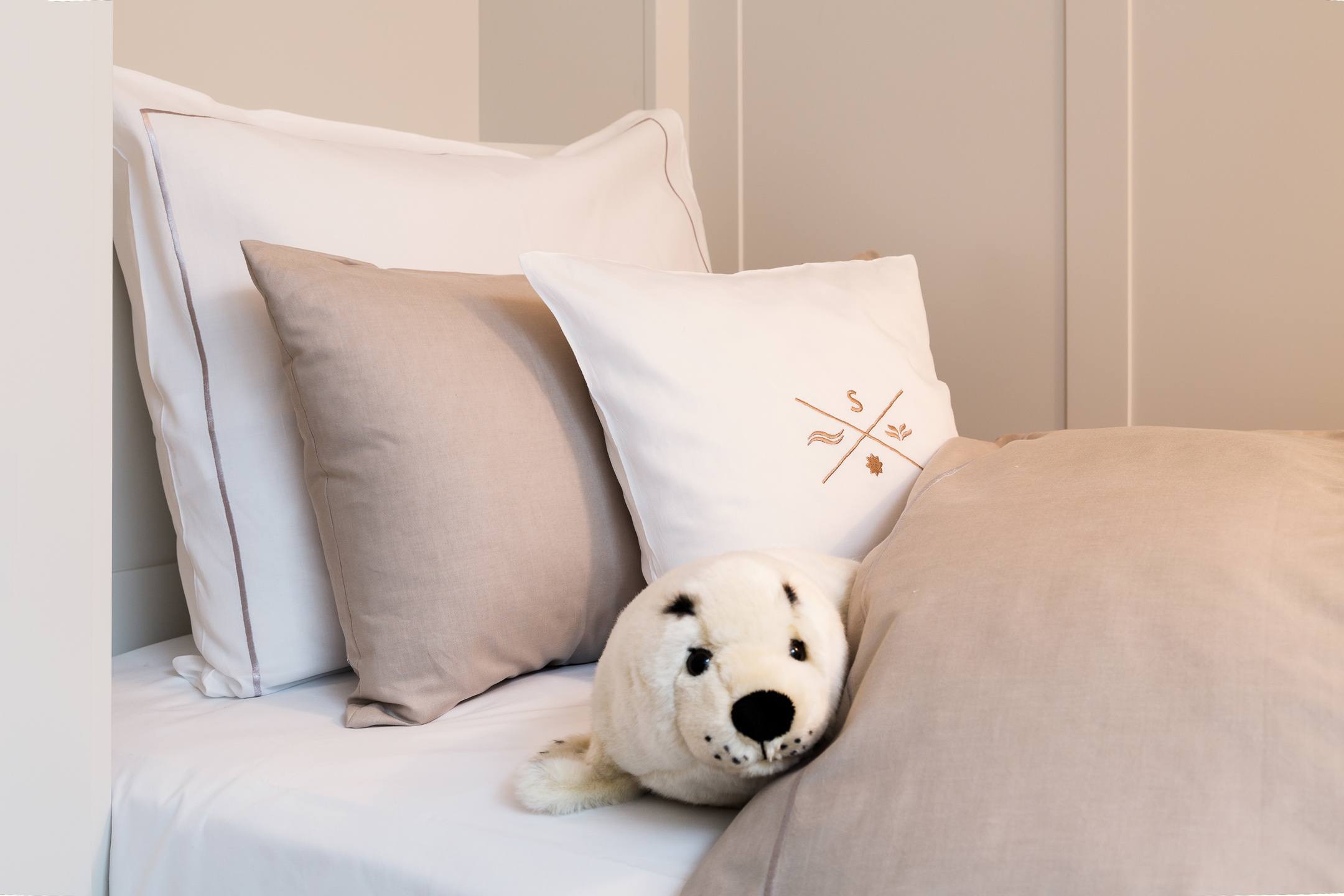 Luxuriöses Bett mit weißen und beigen Kissen, dekoriert mit einem Plüschrobben, im Severin*s Resort & Spa auf Sylt.