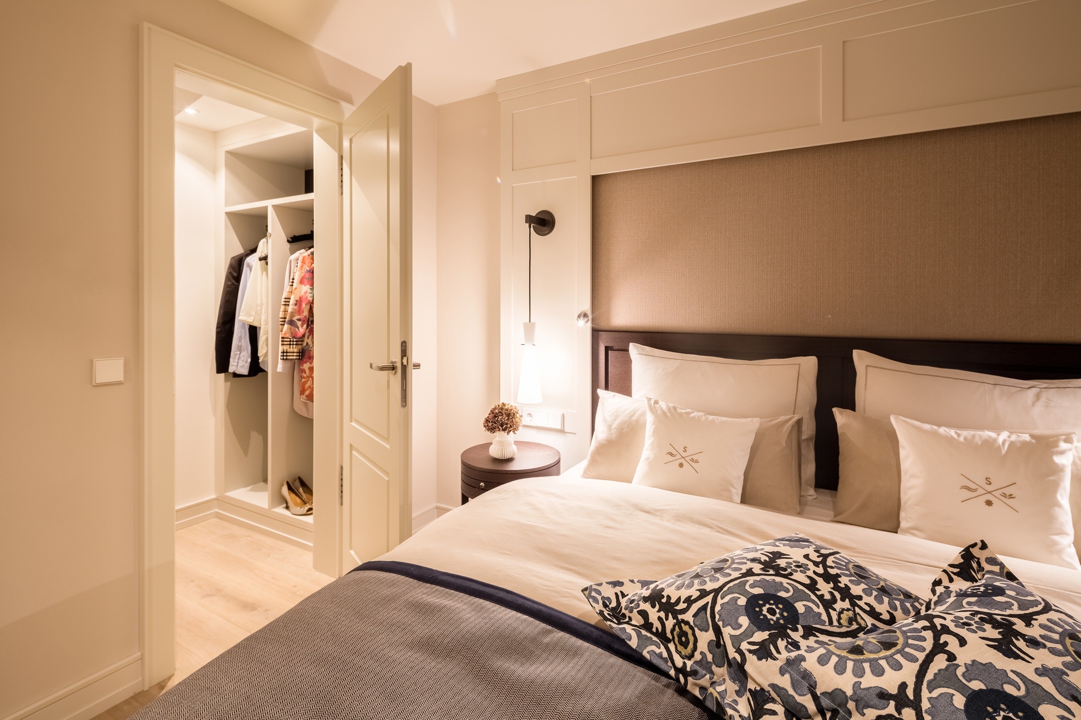 Elegant hotel room with cozy bed, fine bed linen, stylish pillows and open closet in the background.
