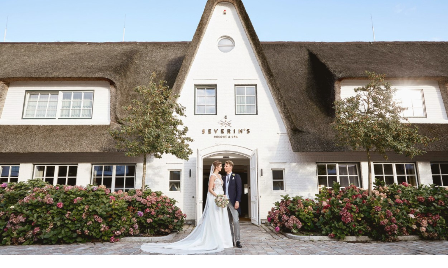 Brautpaar vor dem eleganten Eingang des Severin*s Resort & Spa, umgeben von blühenden Hortensien.
