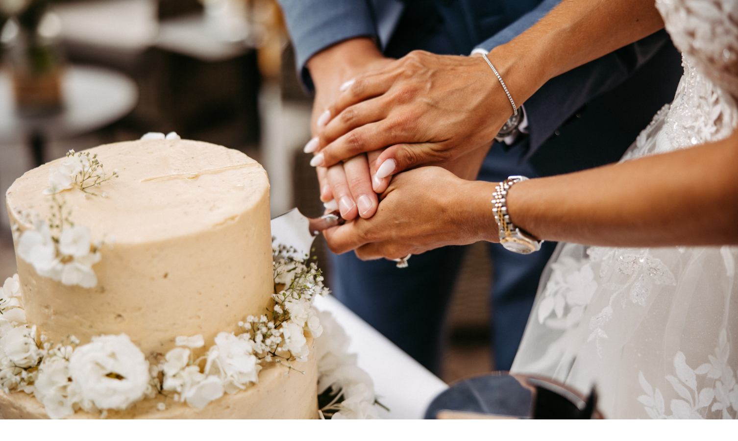 Hände eines Paares schneiden gemeinsam eine mit Blumen verzierte Hochzeitstorte an.