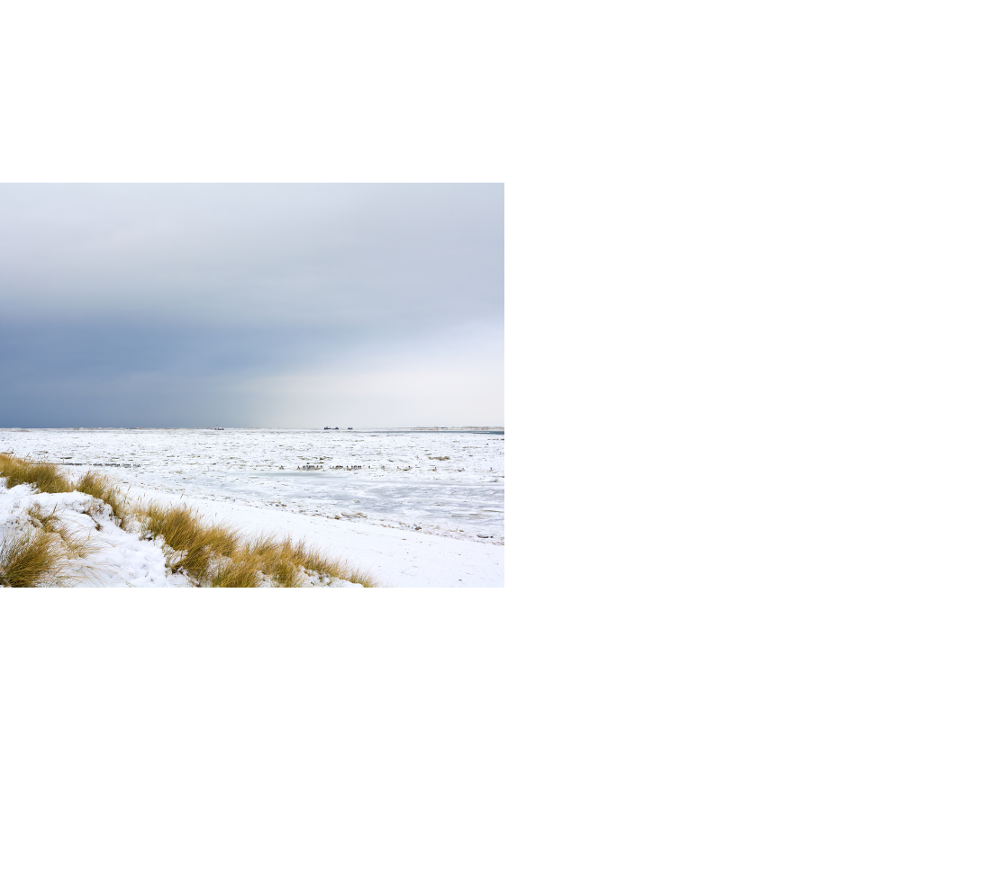 Verschneite Dünen und gefrorenes Meer unter bewölktem Himmel auf Sylt.