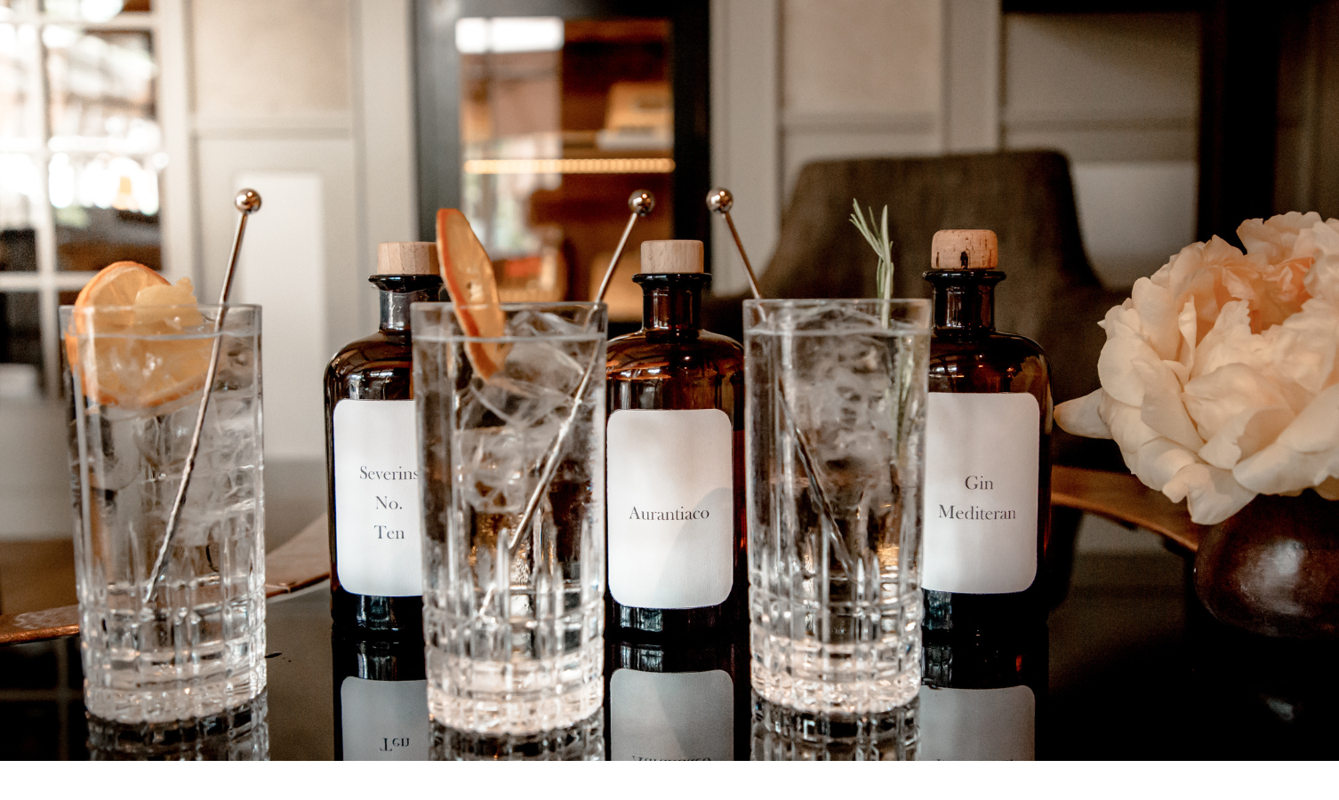 Vier Gläser mit Eis und Zitrus, flankiert von Gin-Flaschen, auf einem eleganten Tisch im Severin*s Resort & Spa.