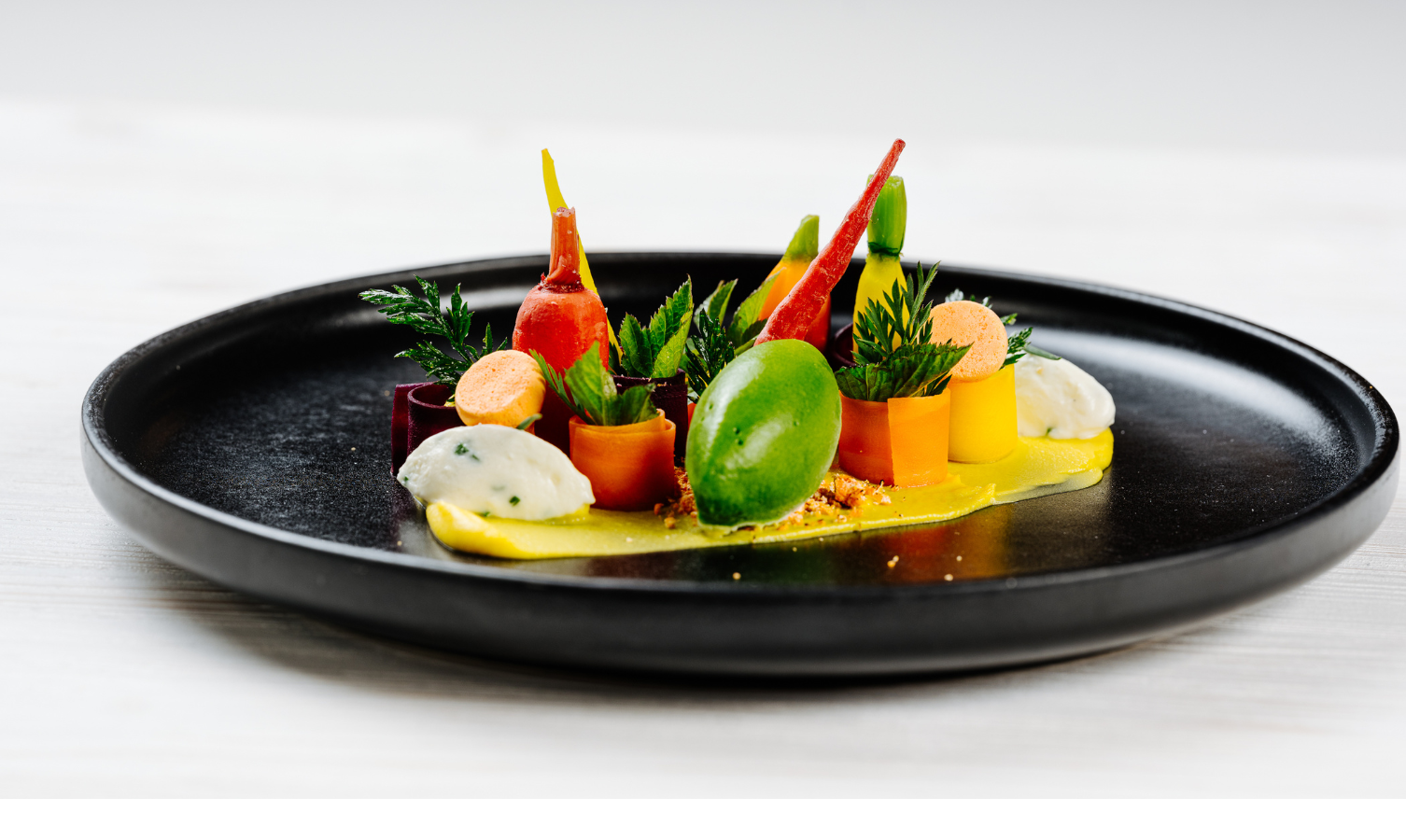 Elegantes, buntes Gourmetgericht auf schwarzem Teller im Severin*s Resort & Spa, kreativ angerichtet mit Gemüse und Kräutern.