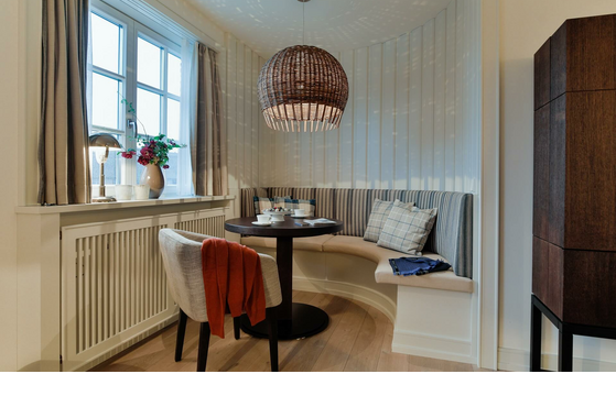 Cozy seating area with round table, upholstered bench, cushions and hanging lamp at Severin*s Resort & Spa on Sylt.