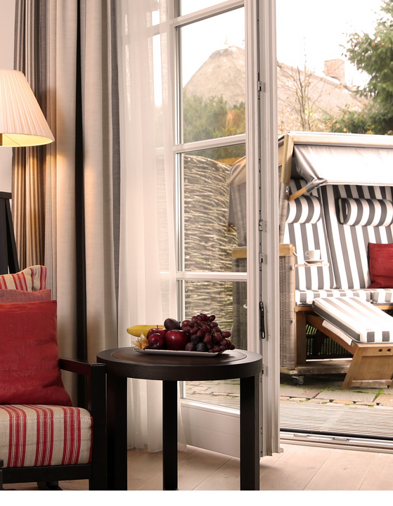 Gemütlicher Wohnbereich mit Sessel, Tisch und Obst, Blick auf Terrasse mit Strandkorb im Severin*s Resort & Spa auf Sylt.