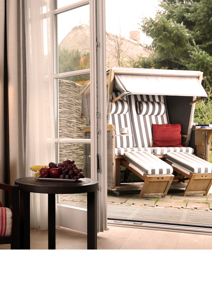 Cozy living area with armchair, table and fruit, view of the terrace with beach chair at Severin*s Resort & Spa on Sylt.