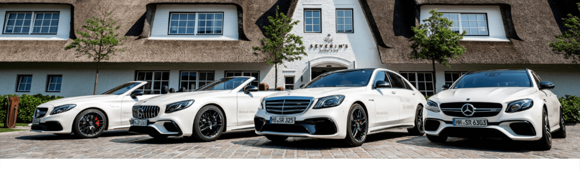 Vier weiße Luxusautos vor dem Eingang des Severin*s Resort & Spa auf Sylt, mit Reetdach und gepflegtem Ambiente.