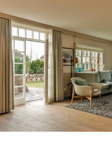 Helles Wohnzimmer im Severin*s Resort & Spa mit Sofa, Sesseln, Teppich und Zugang zu einem Garten.
