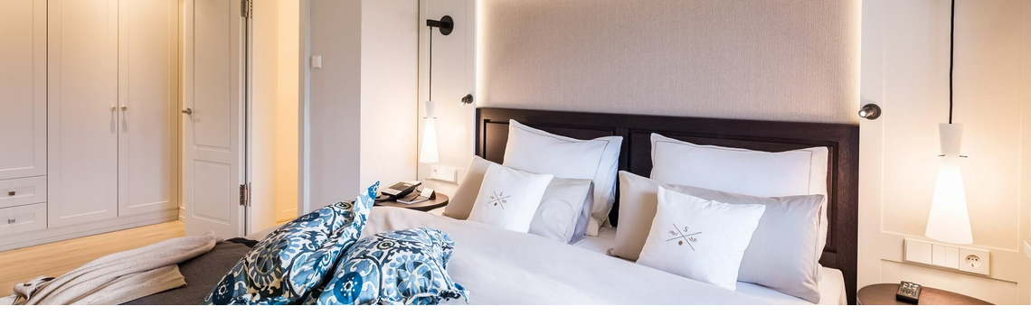 Elegant hotel room with large bed, stylish pillows and modern lighting at Severin*s Resort & Spa on Sylt.