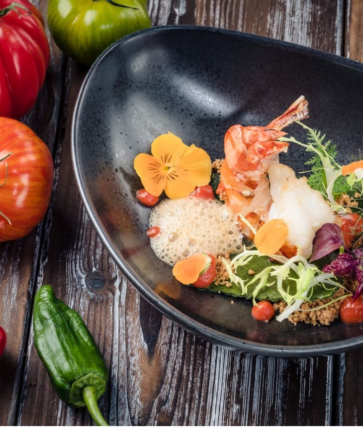 Healthy food Gourmet plate with prawns, salad and edible flowers, stylishly arranged on dark crockery, surrounded by fresh tomatoes.