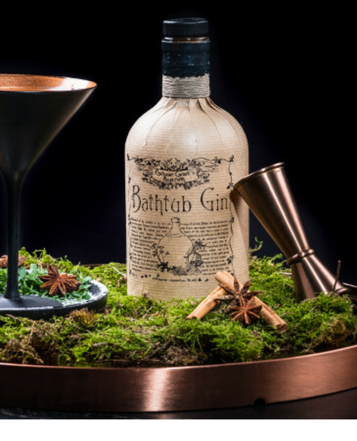 Gin bottle, copper mug and cocktail glass on moss decorated with star anise.