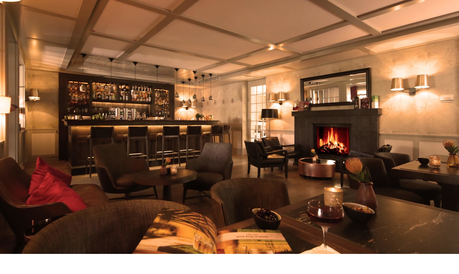 Cozy hotel bar with fireplace, elegant seating and illuminated bar at Severin*s Resort & Spa on Sylt.