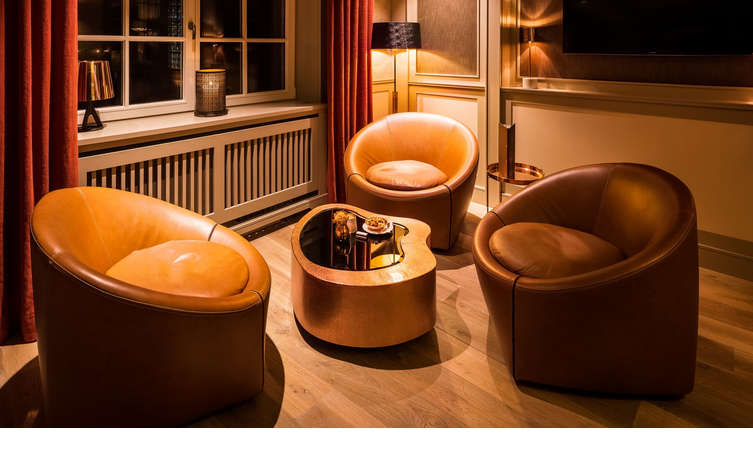 Cozy lounge with three brown leather armchairs and an elegant, copper-colored table in warm light.