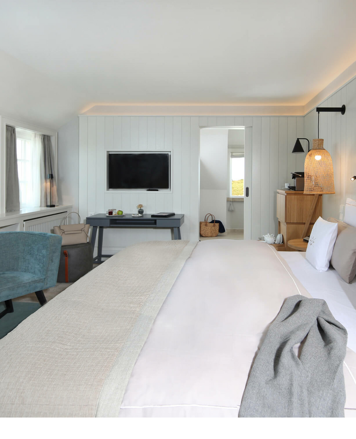 Landhaus-Zimmer im Hotel auf Sylt Bright hotel room with double bed, armchair, desk and TV. Modern, comfortable furnishings with soft colors.