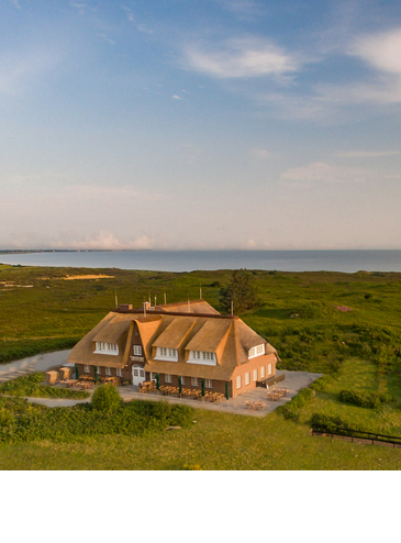 Reetgedecktes Hotel Landhaus Severin*s auf Sylt, umgeben von grüner Landschaft, mit Blick auf das Meer.