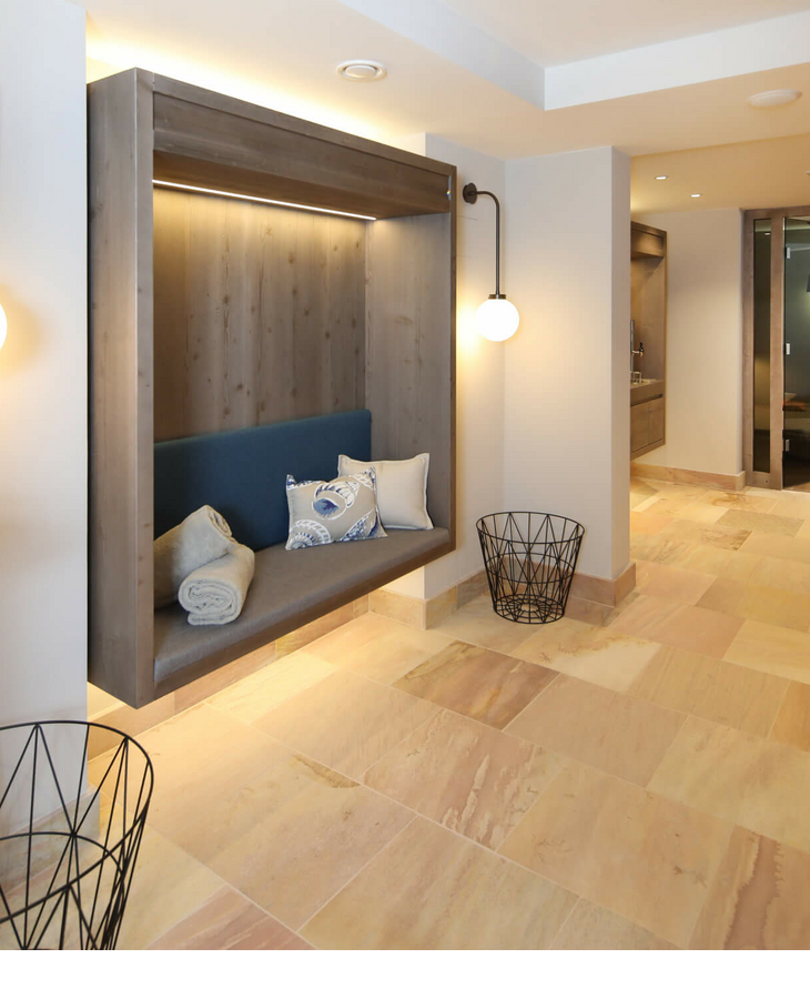 Wellnessbereich im Landhaus Severin*s Morsum Kliff auf Sylt Modern hotel corridor with wooden bench, cushions, blankets, warm light and view into a cozy lounge area.