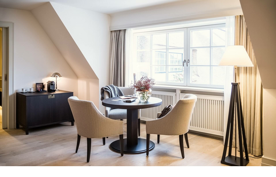 Cozy sitting area with round table, two armchairs, large window front and stylish floor lamp at Severin*s Resort & Spa.