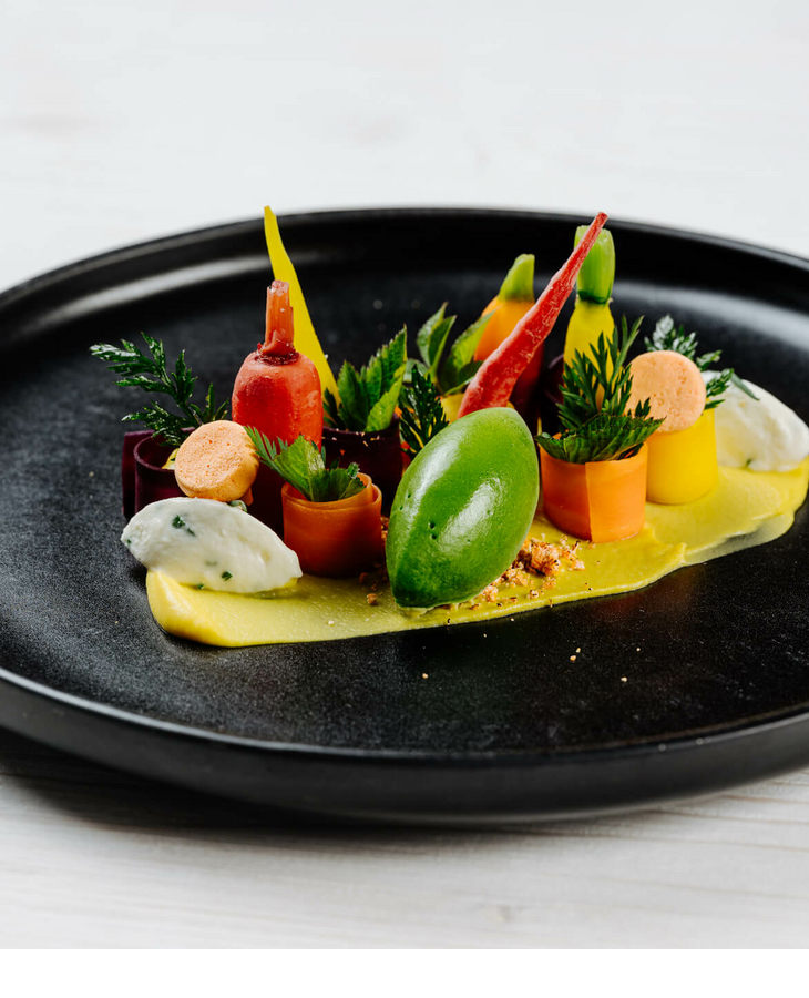 Ein kunstvoll angerichtetes Gourmetgericht mit buntem Gemüse auf schwarzem Teller.