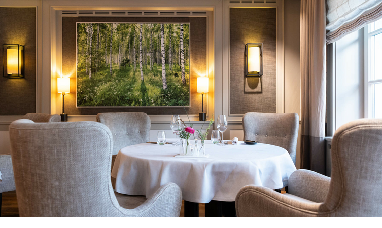 Elegantes Restaurant mit gedecktem Tisch, bequemen Sesseln und einem Gemälde von Birkenwald an der Wand.