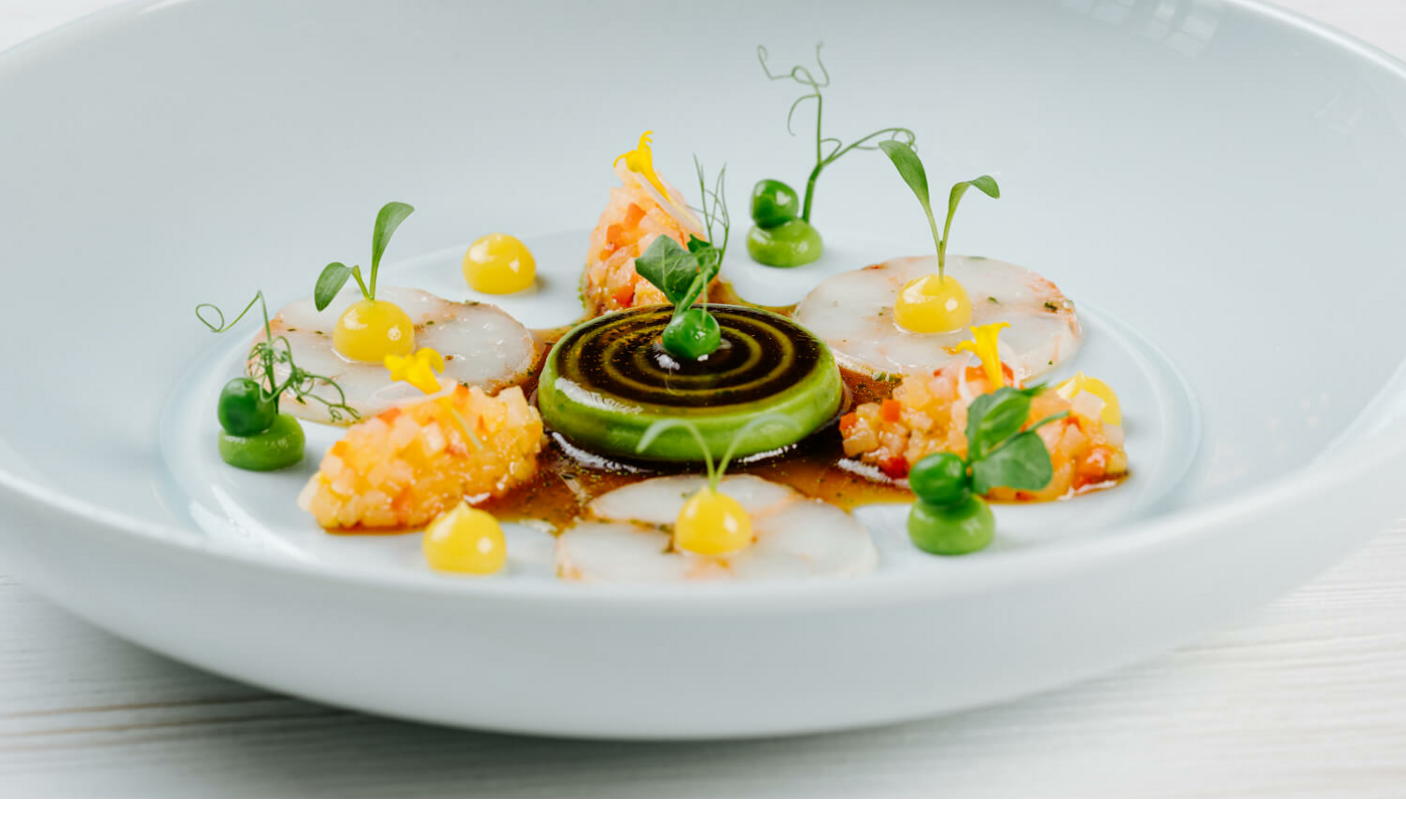 Gourmetgericht mit kunstvoll angerichteten Zutaten, darunter grüne Creme, gelbe Tupfer und feine Scheiben auf weißem Teller.