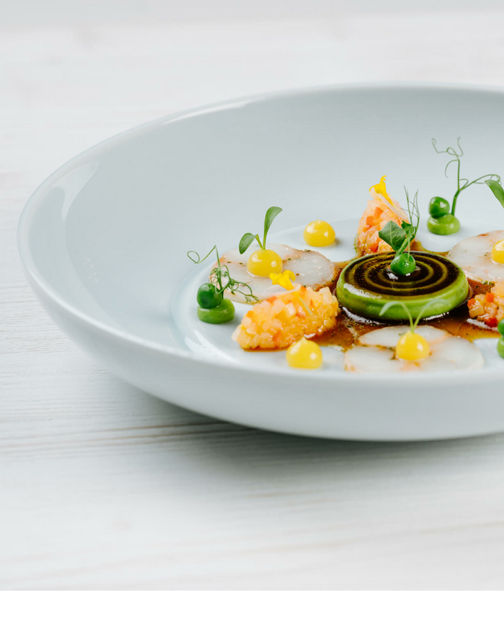 Gourmet dish with artfully arranged ingredients, including green cream, yellow dots and fine slices on a white plate.