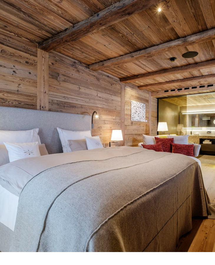 Senior Suite im Hotel Severin*s – The Alpine Retreat in Lech Gemütliches Hotelzimmer mit Holzwänden, großem Bett, moderner Beleuchtung und Blick ins luxuriöse Badezimmer.