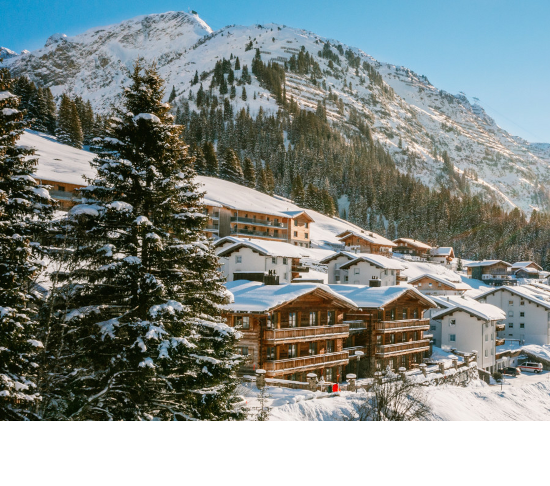 Verschneite Alpenlandschaft mit Sonne über Hotel Severin*s in Lech, umgeben von Bergen und Bäumen.