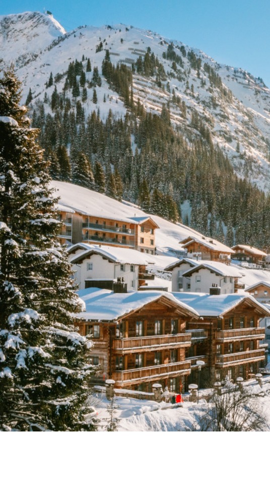 Verschneite Alpenlandschaft mit Sonne über Hotel Severin*s in Lech, umgeben von Bergen und Bäumen.