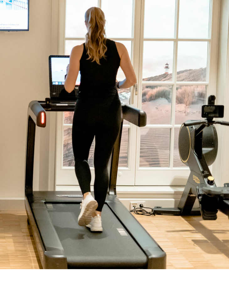 A woman runs on a treadmill in a bright fitness room with a television
