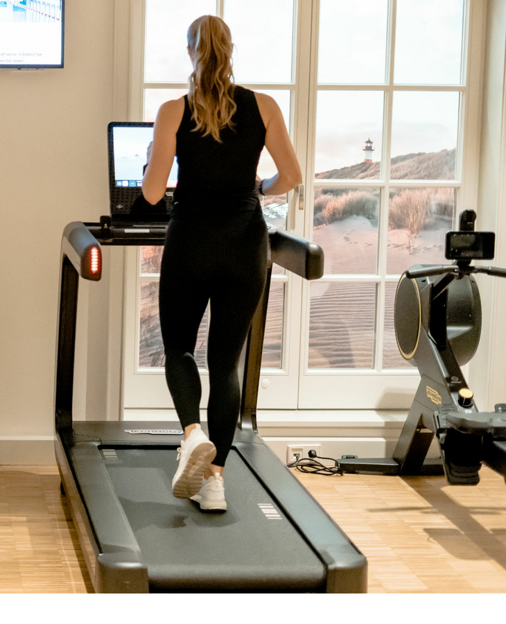 Eine Frau läuft auf einem Laufband in einem hellen Fitnessraum mit Fernseher