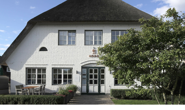 Weißes Reetdachhaus des Severin*s Resort & Spa auf Sylt, mit Terrasse und Garten im Vordergrund.