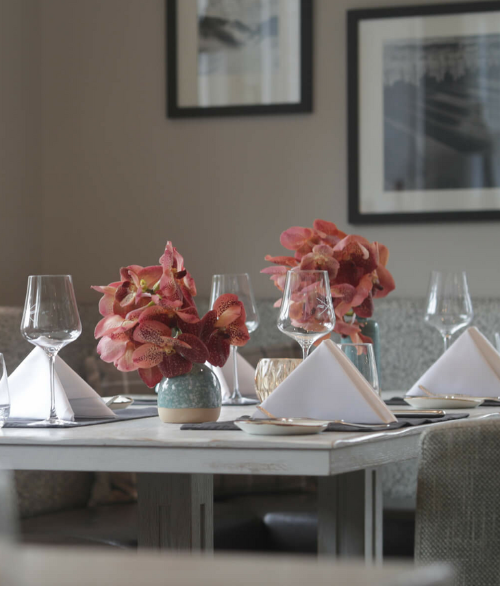 Elegantes Restaurant mit gedecktem Tisch, Blumenarrangements und weichen Sitzbänken im Severin*s Resort & Spa auf Sylt.