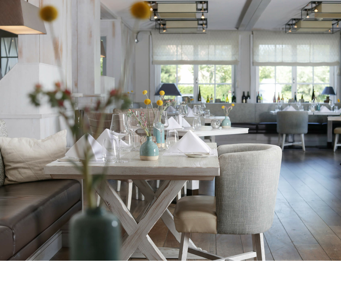 Elegant restaurant with laid tables, stylish decoration and large windows at Severin*s Resort & Spa on Sylt.