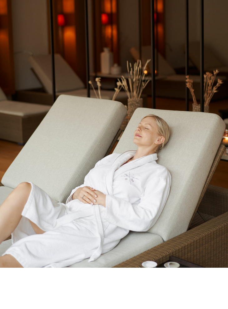 A woman in a bathrobe lies on a padded lounger in the day spa area