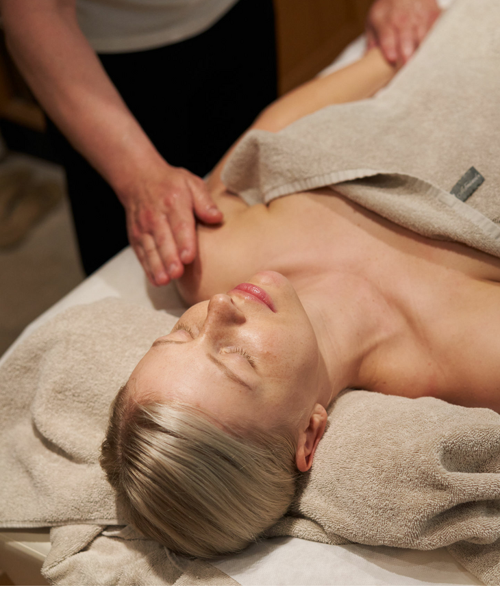 A woman lies on her back on a massage bench and her left arm is massaged