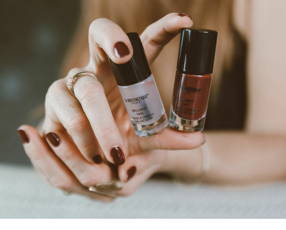 Frau mit rot lackierten Nägeln hält zwei Nagellackfläschchen in der Hand.