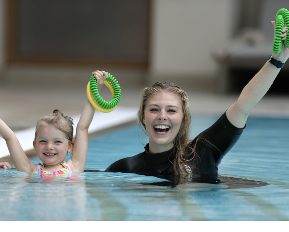 Erwachsene und Kind lächeln im Pool des Severin*s Resort & Spa, halten bunte Schwimmringe hoch.