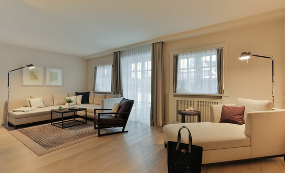 Elegant hotel room with beige sofa area, stylish furniture and large windows with curtains.