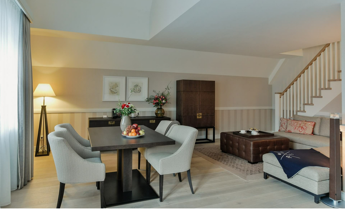 Elegant living room at Severin*s Resort with dining table, comfortable armchairs, sofa, flowers and staircase.