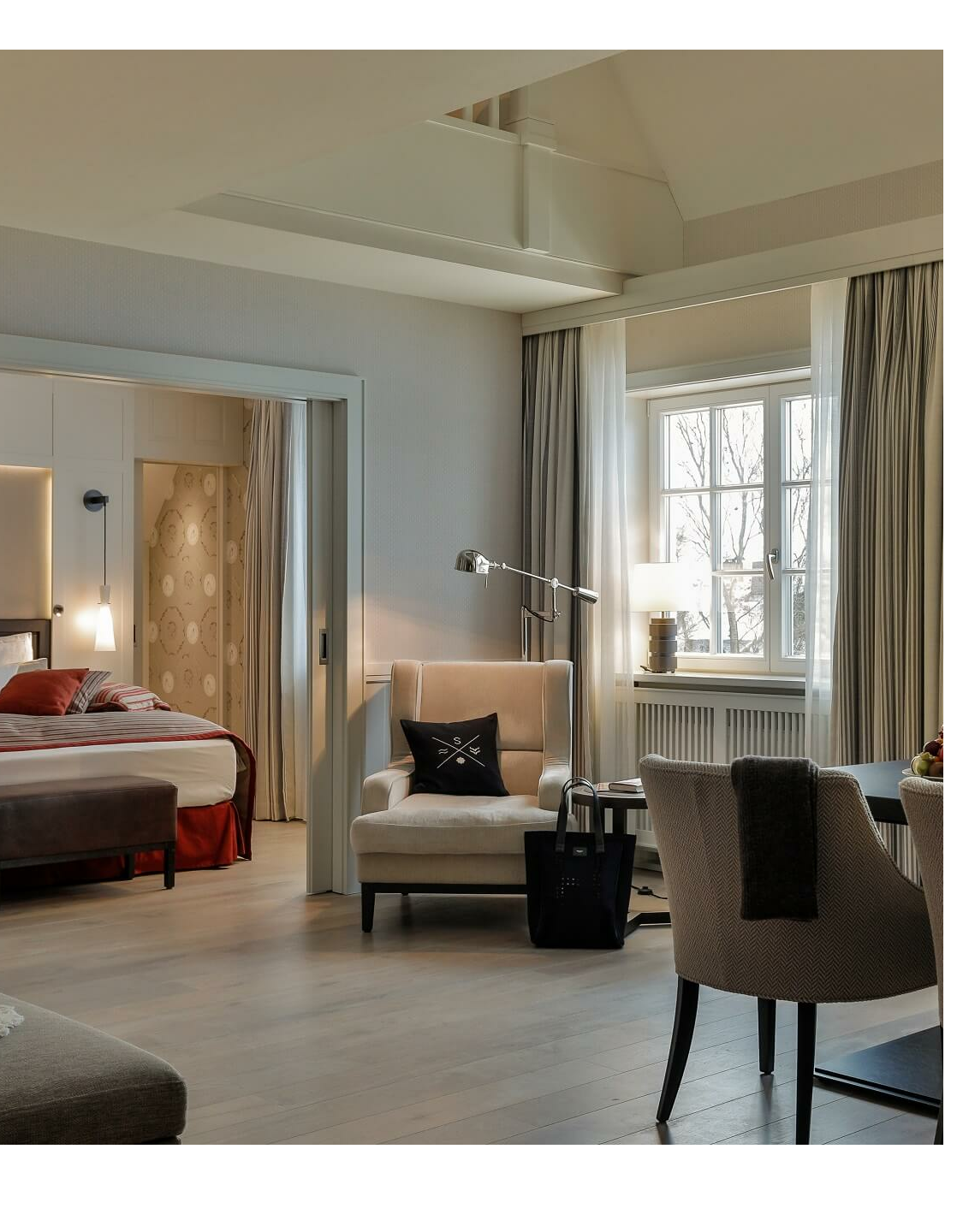 Luxurious suite with elegant living area, dining table, cozy armchair and view into the bedroom at Severin*s Resort.